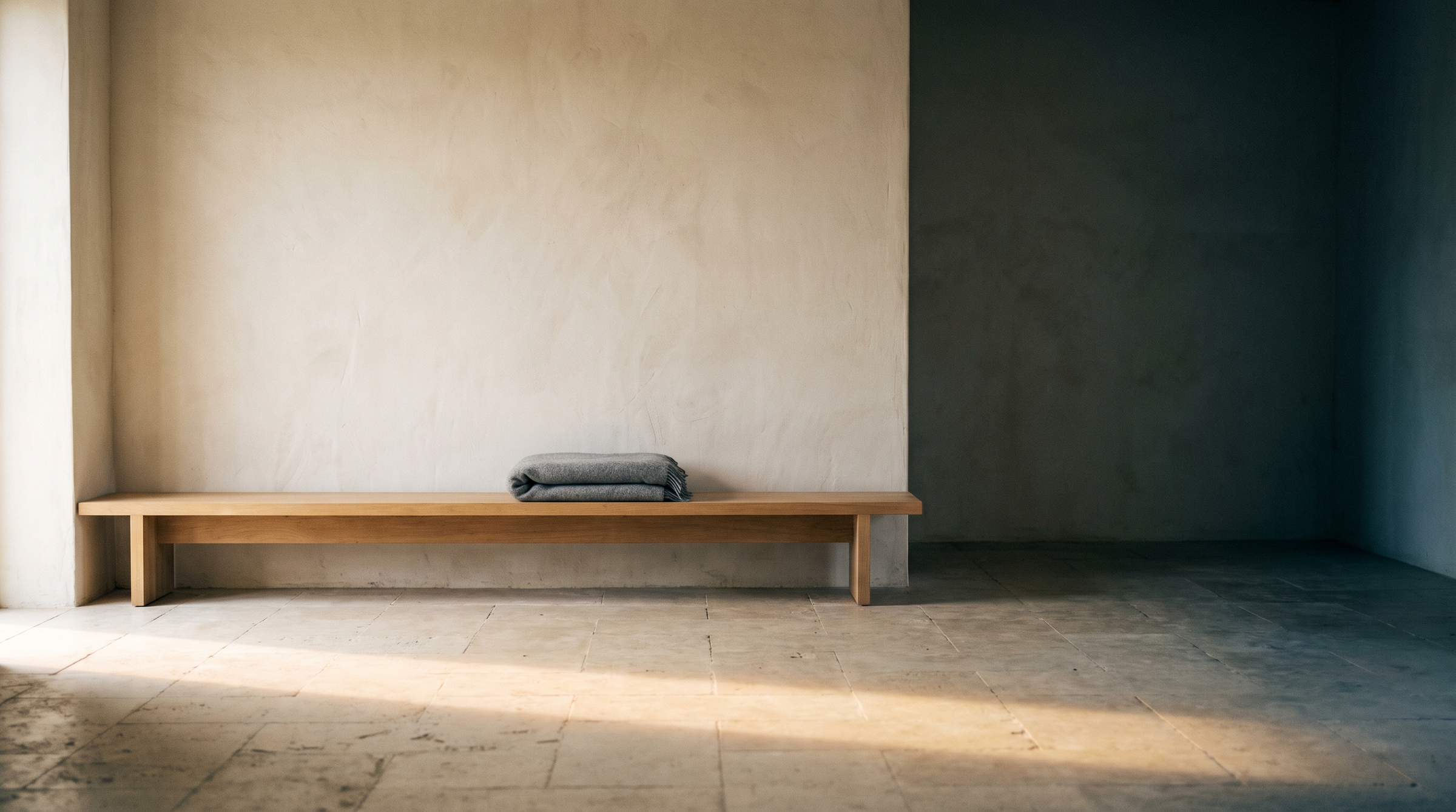 A bare wall and a low wooden bench with a folded blanket